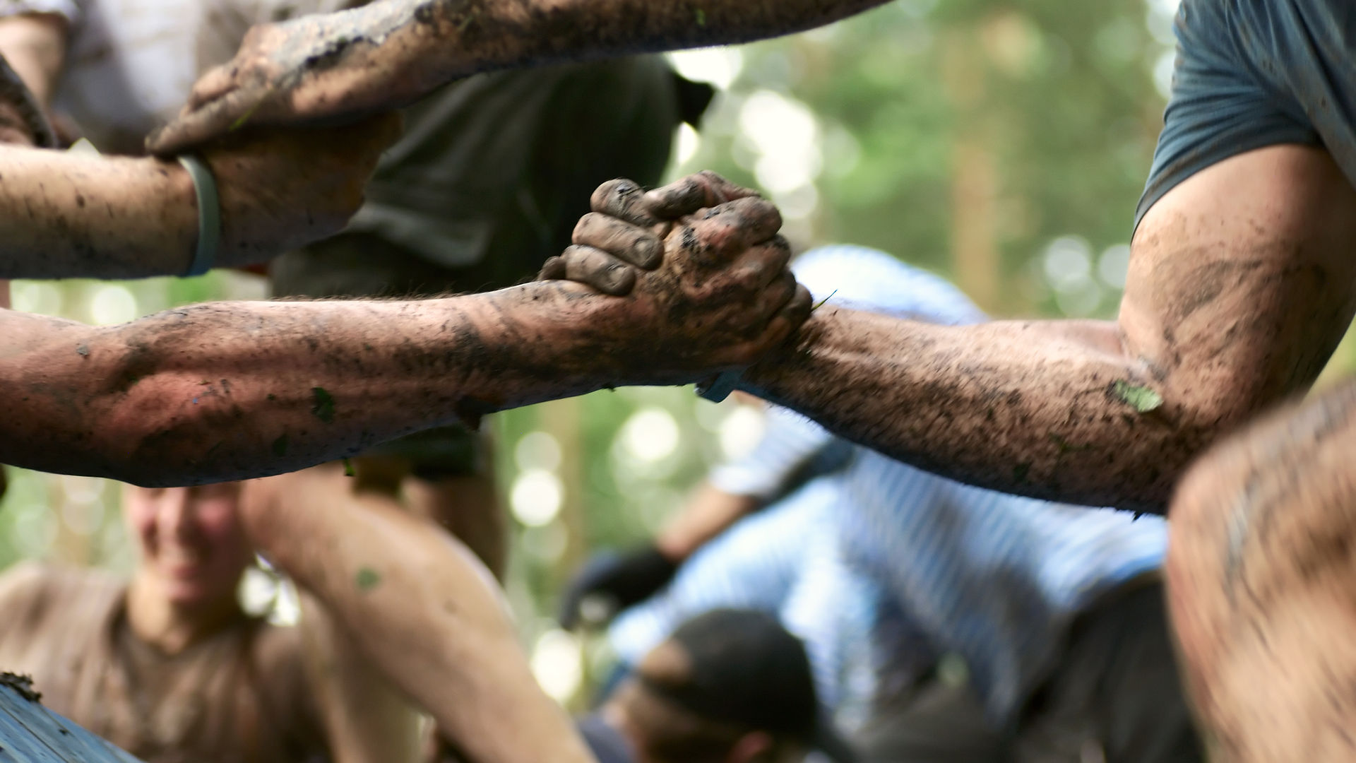 A circle of muddy hands clasping arms together — a community of people supporting one another in recovery